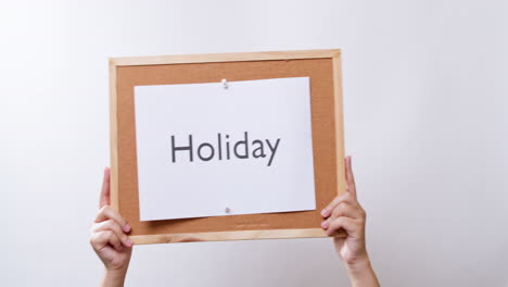 Woman's-hand-shows-the-paper-on-board-with-the-word-Holiday-in-white-studio-background-with-copy-space