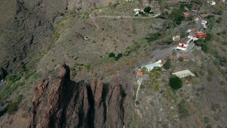 Aerial-Tilt-Downward-Revealing-Mountainside-Village-by-Pointed-Rock-Formation,-Daytime