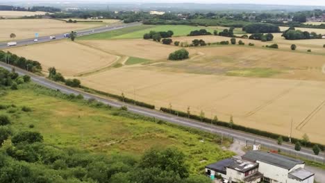 Aerial-view-across-agricultural-meadows-and-fields-in-rural-UK-countryside-to-M62-motorway-traffic