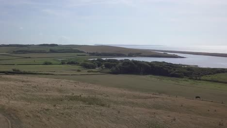 Low-forward-tracking-aerial-down-a-hill-towards-the-fleet-lagoon-at-the-west-end-of-Chesil-Beach