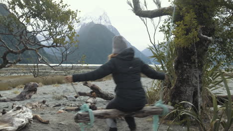 Reveal-shot-of-girl-swinging-on-wooden-swing-with-snow-capped-peaks-and-mountains-in-the-background