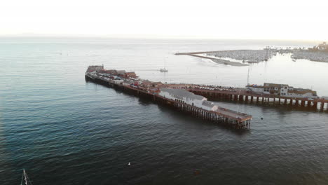 Aerial-drone-shot-over-Stearns-Wharf-pier-and-sailboats-in-the-blue-ocean-near-Santa-Barbara-Harbor,-California