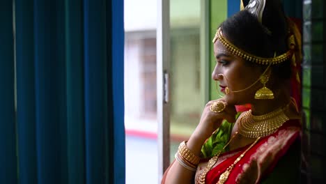 Newly-wed-Romantic-and-beautiful-Indian-bride-looks-outside-through-window-on-rainy-evening