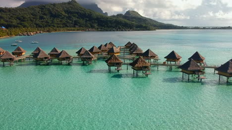Aerial-wide-shot-of-overwater-bungalows-in-a-turquoise-lagoon-with-Mountains-in-the-background,-Bora-Bora,-French-Polynesia