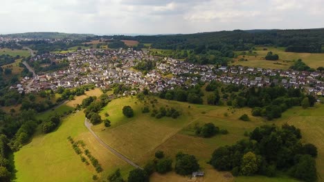 Flight-with-a-DJI-Phantom-4-Drone-towards-a-rural,-german-village-located-in-a-beautiful-forest-and-field-area-with-sunrays-lighting-up-the-ground