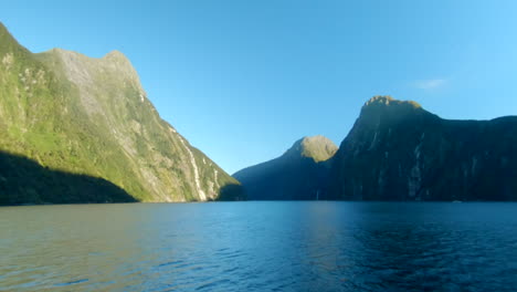 wide-shot-of-the-first-sunbeams-during-sunrise-hitting-the-cliffs-of-the-mountains-in-a-fiord,-Milford-Sound,-New-Zealand