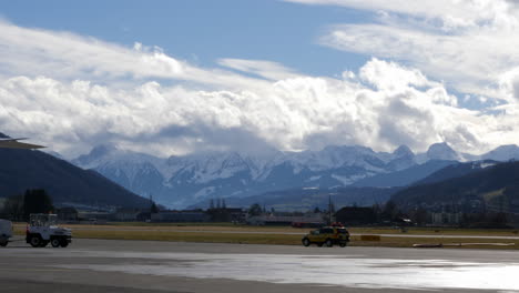 A-corporate-jet-taxiing-behind-a-follow-me-car-on-an-airfield,-snowy-mountains-in-the-background