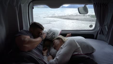 SLOWMO---Young-attractive-couple-in-bed-waking-up-in-motorhome-by-Lake-Wakatipu,-Queenstown,-New-Zealand