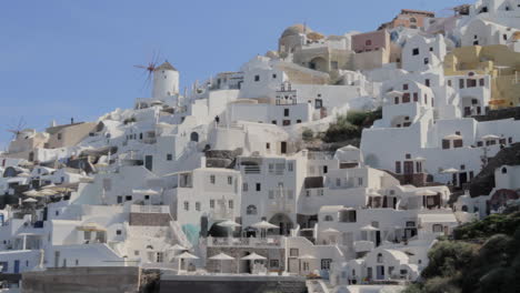 Wide-shot-of-holiday-homes-and-villas-in-Oia,-Santorini,-with-a-windmill