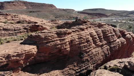 Drone-flies-over-red-rocks,-person-sitting-on-top-of-the-rocks-looking-down
