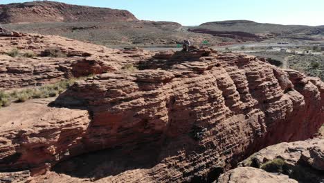 Drohne-Fliegt-über-Rote-Felsen,-Person-Sitzt-Auf-Den-Felsen-Und-Schaut-Nach-Unten