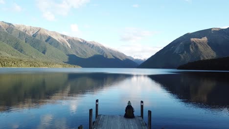 aerial-view-flying-slowly-over-Jetty-into-the-calm-mirror-like-water-in-Lake-Rotoiti,-Nelson,-New-Zealand