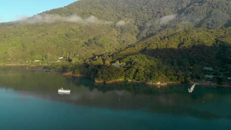 SLOWMO---Sunrise-aerial-flying-over-sea-and-anchored-boats-towards-bay-and-house-on-hill-in-Marlborough-Sounds,-New-Zealand