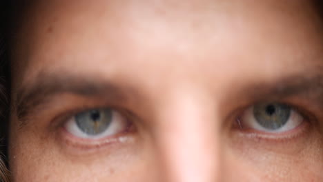 Close-up-of-a-young-man-initially-out-of-focus,-walking-and-opening-his-light-blue-eyes,-staring-at-the-camera-without-blinking