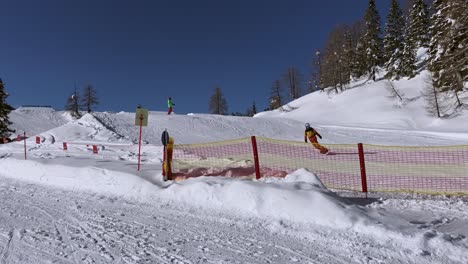 Toma-Amplia-En-Cámara-Lenta-De-Un-Hombre-Que-Hace-Snowboard-Sobre-Un-Salto-De-Esquí-Y-Vuela-Un-Poco-En-El-Aire-Antes-De-Aterrizar-Y-Deslizarse-Sobre-El-Snowboard