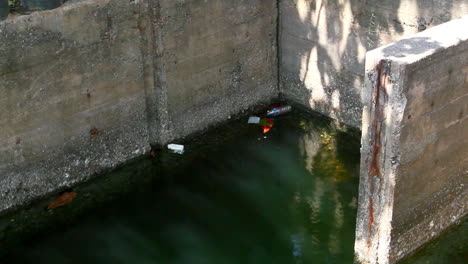 Tiro-Medio-Bloqueado-De-La-Construcción-De-Hormigón-De-Una-Puerta-De-Inundación-En-El-Lago-Nai-Harn-Y-La-Playa-Medio-Llena-De-Agua-De-La-Laguna-Y-Basura-Plástica-Al-Azar