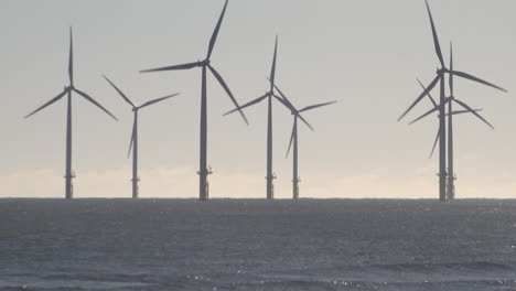 Turbinas-Eólicas-Girando-En-Una-Granja-En-Alta-Mar-Frente-A-La-Costa-De-Hartlepool-En-El-Mar-Del-Norte-Mientras-Las-Olas-Rompen-En-La-Orilla