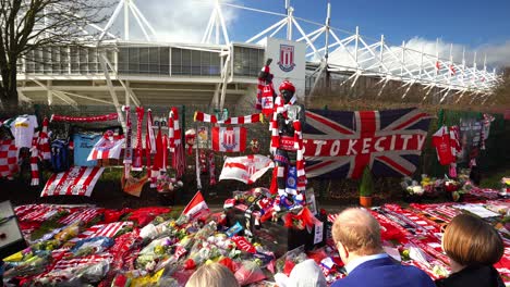 People-pay-their-respects-at-the-Gordon-Banks-statue-by-the-Stoke-City-stadium,-people-signing-shirts,-scarves,-flags-and-the-book-of-remembrance