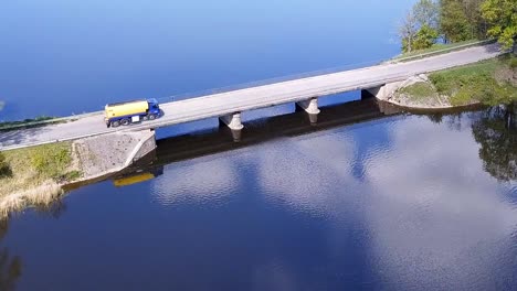 Aerial-shot-of-a-fuel-truck-driving-on-a-bridge-over-a-lake