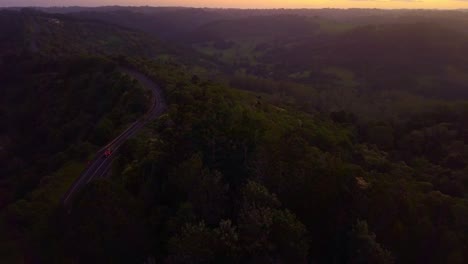 Revealing-smooth-aerial-shot-of-a-road-through-tropical-forest-valley-in-Kondalilla,-Australia-during-sunset