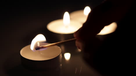 Eine-Kleine-Kerze-Wird-Mit-Einem-Streichholz-Angezündet,-Im-Hintergrund-Eine-Gruppe-Brennender-Kerzen