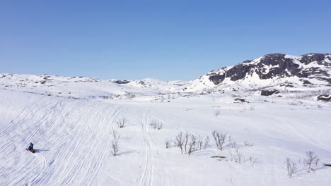 Vista-Aérea-De-La-Persona-En-Moto-De-Nieve-En-El-Paisaje-Montañoso-Nevado