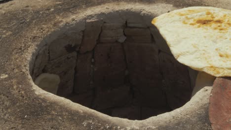 Refugee-woman-sticks-dough-to-side-of-Tandoor-oven-to-bake-bread-at-refugee-camp-CLOSE-UP-OVEN