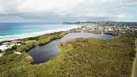 Drone-rising-up-revealing-coastal-tea-tree-lake-with-beach-in-background