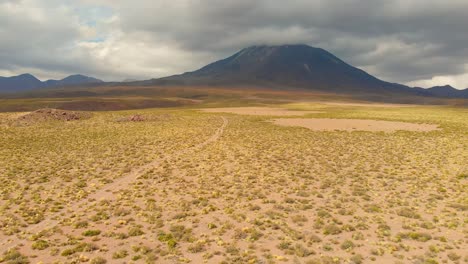 Aerial-cinematic-shot-following-a-dirt-road-distancing-from-Lascar-Volcano-in-the-Atacama-Desert,-Chile,-South-America