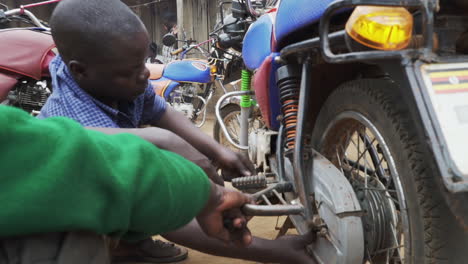 Mechanics-working-on-a-motorcycle-at-local-outdoor-mechanics-workshop-in-some-Ugandan-village,-Uganda-Africa