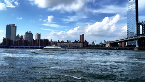 Seas-Freak-Boat-cruise-vessel-ferry-in-the-East-river-with-lower-manhattan-skyline-in-the-background-and-manhattan-bridge-on-the-right-with-dramatic-clouds