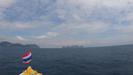 View-from-boat-on-sea-with-Thai-flag-flapping-in-the-wind-and-phi-phi-island-in-the-distance,-Thailand-in-4K-59