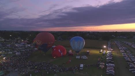 Luftaufnahme-Eines-Heißluftballonfestivals-Bei-Nacht,-Bei-Dem-Propan-Abgefeuert-Wird-Und-In-Einer-Sommernacht-Ein-Nächtliches-Leuchten-Erzeugt
