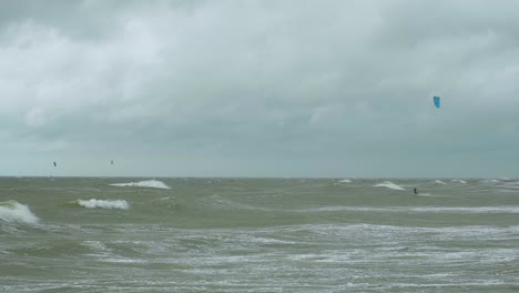 Surfistas-De-Kite-surf-Navegando-En-Las-Grandes-Olas-Del-Mar-Báltico-En-La-Playa-De-Liepaja-Karosta,-Día-De-Otoño-Nublado,-Tiro-Ancho-En-Cámara-Lenta