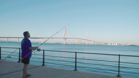 Spanish-man-casting-fishing-rod-by-Bay-of-Cadiz-Bridge,-Slow-Motion