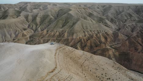 breathtaking-tilt-down-on-a-car-standing-at-a-cliff,-Judean-desert,-Israel,-aerial-shot