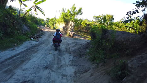 Imágenes-De-Una-Motocicleta-De-Dos-Ruedas-En-Marcha-Cargada-Con-Un-Pasajero-Y-Equipaje-En-Una-Carretera-Accidentada