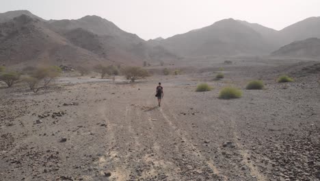 Aerial-revealing-shot-from-drone-of-an-young-male-walking-in-a-rocky-desert-valleys-in-Hatta,-United-Arab-Emirates