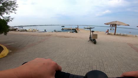 Vista-De-Cámara-Desde-Un-Patinete-Eléctrico-Que-Recorre-La-Calle-Hasta-La-Playa-En-Un-Día-De-Verano-Con-Vistas-A-Otro-Patinete-Estacionado