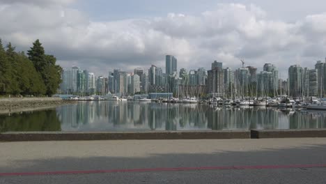 Vista-Panorámica-Del-Centro-De-La-Ciudad-De-Vancouver-En-Canadá-Con-Muchos-Yates-En-El-Puerto-De-Vancouver-vista-Desde-El-Parque-Stanley-Y-Reflejo-De-La-Ciudad-En-La-Superficie-Del-Lago