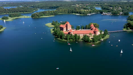 Luftaufnahme:-Rotierende-Höhenaufnahme-Der-Burg-Trakai-Mit-Booten-Und-Yachten,-Die-Auf-Dem-See-Um-Die-Insel-Der-Burg-Trakai-Kreisen,-Mit-Wald-Und-Bäumen-Im-Hintergrund