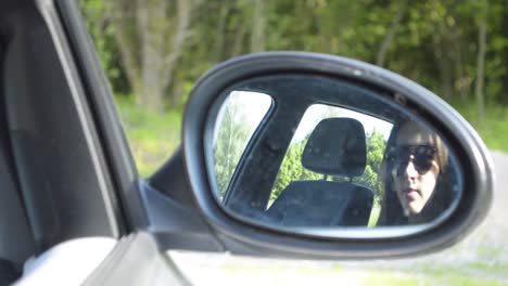 Young-girl-with-sunglasses-sitting-in-the-car-looking-in-the-mirror-while-rolling-the-window-up,-SLOMO