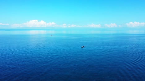 Blaues-Meerwasser,-Das-Weiße-Wolken-Und-Hellen-Himmel-Reflektiert,-Friedliche-Meereslandschaft-Mit-Boot,-Das-Nahe-Der-Küste-Einer-Tropischen-Insel-In-Indonesien-Schwimmt