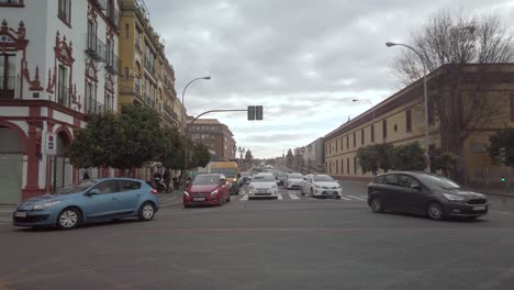 Cars-drive-toward-camera-and-turn-at-intersection-in-Seville,-Spain