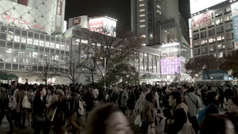 Hundreds-of-people-on-the-Shibuya-crossing-at-night-with-illuminated-buildings-and-billboards,-stable-handheld-shot