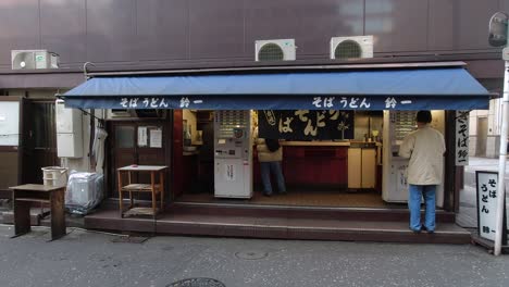 Vorderansicht-Eines-Straßenimbissstandes-Auf-Der-Rückseite-Eines-Gebäudes-In-Tokio,-Japan,-Mit-Kaufenden-Kunden-–-Weitwinkelaufnahme