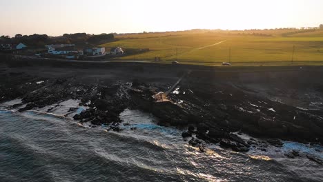 The-drone-is-flying-backwards-and-rising-in-height-to-show-the-beautiful-rocky-beach-of-Malahide-during-a-golden-hour