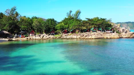 Tranquil-bay-with-turquoise-shallow-lagoon-washing-beautiful-rocky-shoreline-of-tropical-island,-beach-cabins-under-green-trees-in-Vietnam