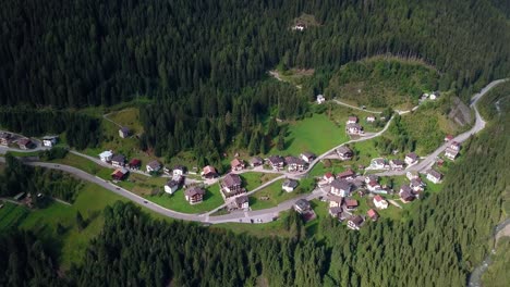 Mountain-village-at-the-Dolomite-area-in-northern-Italy-with-roads-passing-through-buildings-and-homes,-cars-driving-by,-Aerial-drone-top-view-shot