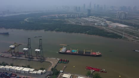 Aerial-view-of-Saigon-River-featuring-the-deep-water-port-facility,-shipping,-wetlands-and-elements-of-the-city-skyline-on-a-day-of-high-air-pollution